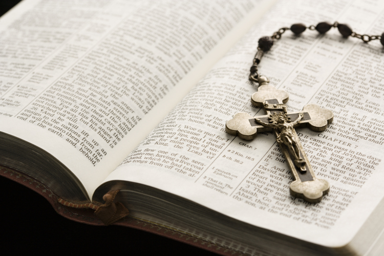 Rosary with crucifix lying on open Bible.